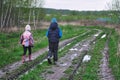 Two kids brother and sister walks on dirty countryside road after rain