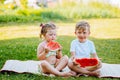 Two kids eat watermelon in the garden. Kids eat fruit outdoors. Healthy snack for children.Toddlers girl and boy enjoy