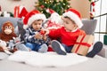 Two kids holding gift sitting on sofa by christmas tree at home Royalty Free Stock Photo