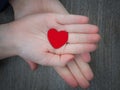 Two kids holding red heart in hand over solid wooden background