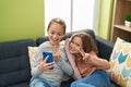 Two kids make selfie by smartphone sitting on sofa at home