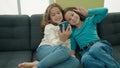 Two kids make selfie by smartphone sitting on sofa at home