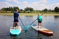 Two Kids Outside on Lake Learning to Stand Up Paddle Board on Summer Day