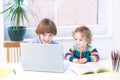 Two kids playing with laptop sitting at white desk Royalty Free Stock Photo