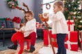 Two kids playing with reindeer rocking and horse toy standing by christmas tree at home Royalty Free Stock Photo