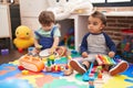 Two kids playing xylophone and tambourine sitting on floor at kindergarten