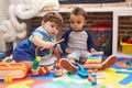 Two kids playing xylophone and tambourine sitting on floor at kindergarten