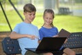 Two kids, teenager boy holding laptop computer and young girl with digital tablet studying together outdoors Royalty Free Stock Photo