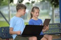 Two kids, teenager boy holding laptop computer and pretty young girl with digital tablet studying together outdoors Royalty Free Stock Photo