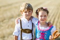 Two kids in traditional Bavarian costumes in wheat field. German children eating bread and pretzel during Oktoberfest Royalty Free Stock Photo