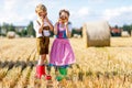 Two kids in traditional Bavarian costumes in wheat field. German children eating bread and pretzel during Oktoberfest