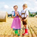 Two kids in traditional Bavarian costumes in wheat field. German children eating bread and pretzel during Oktoberfest Royalty Free Stock Photo