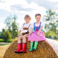 Two kids in traditional Bavarian costumes in wheat field. German children sitting on hay bale during Oktoberfest. Boy Royalty Free Stock Photo