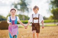 Two kids in traditional Bavarian costumes in wheat field. German children sitting on hay bale during Oktoberfest. Boy