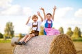 Two kids in traditional Bavarian costumes in wheat field. German children sitting on hay bale during Oktoberfest. Boy