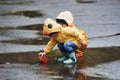 Two kids in yellow waterproof cloaks and boots playing with handmade paper boat outdoors after the rain together Royalty Free Stock Photo