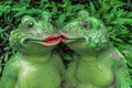 Two kissing frogs decor sculpture in garden backyard. Love story concept. Green toads in front of leaves of bush or shrub Royalty Free Stock Photo