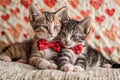 Two kittens wearing red bow ties sitting on a couch with a heart patterned blanket