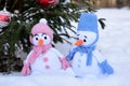 Two knitted Christmas snowmen, a boy and a girl, stand under a decorated Christmas tree outside Royalty Free Stock Photo