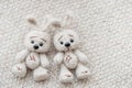 Two knitted white hares are lying on a light knitted handmade fabric