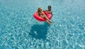 Two ladies in bikini are joyfully floating together on a big inflatable ring in blue water