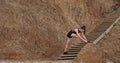 Two ladies in a black sportswear stretching legs on the wooden stents beside the beach background big rocks