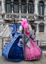 Two ladies holding fans and wearing hand painted masks and ornate blue and pink costumes at Venice C