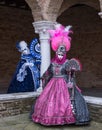 Two ladies wearing brightly colored blue and pink masks and costumes at Venice Carnival.