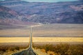 Two lane blacktop highway wavering in the heat stretching into the distant mountains with band of sand intersecting the rough