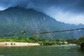 Two laos girls walking across the suspension bridge over the Nam Song River, fantastic cloudy and mountain range backdrop