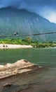 Two laos girls walking across the suspension bridge over the Nam Song River, fantastic cloudy and mountain range backdrop