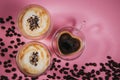 Two large cappuccino cups with grated chacolade on the froth. Next to a cup with coffee in the form of a heart on a pink