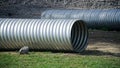 Two large corrugated metal pipes, prepared for installation, lie on a construction site next to a pile of gravel and green grass.