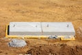 Two large elongated heavy new concrete manhole covers with metal hooks on top of wooden boards surrounded with dry soil