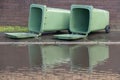 Two large green rubbish bins, lying in UK street, with large puddle, floodwater. After storm