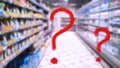 Two large red question marks on abstract blur image of supermarket background. Defocused shelves with products. Grocery shopping.