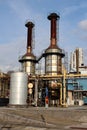 Two large rusted industrial silos surrounded with multiple pipelines at abandoned industrial complex with apartment buildings and Royalty Free Stock Photo