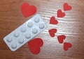 Two large and six small red hearts lie on the surface of a wooden table with a blister of medicine pills, the concept of the need