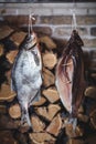 Two large smoked fish hang on background of stacked firewood