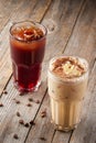 Two large tall glasses with cold coffee sprinkled with almonds and chocolate on wooden table. Coffee beans are scattered