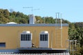 Two large ventilation units on metal platform on top of industrial building surrounded with metal stairs and dense forest in back