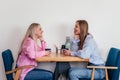 Two laughing mid age women friends sitting in cafe drinking coffee and chatting. Caucasian girls indoors Royalty Free Stock Photo