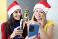 Two laughing women in santa claus hats are looking at smartphone screen and holding glasses of champagne Royalty Free Stock Photo