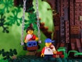 Two Lego child minifigures holding ice cream. The girl is sitting on the swing while the boy is standing near on the ground