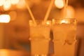 Two lemonades in a glass with ice on chopped lemon wedges. Refreshing cold drink with straws in a cafe. Blurred bokeh