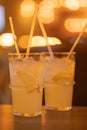 Two Lemonades in a glass with ice cubes on chopped lemon wedges. Refreshing cold drink with straws on the wooden table