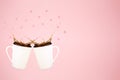 Two levitating coffee mugs with splashes and heart confetti. Coffee concept. Minimal art trend. Solid pink background Royalty Free Stock Photo