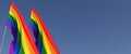 Two LGBT flags on a flagpole on a blue background on the side. The rainbow flag flutters in the wind. Place for text. LGBT