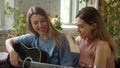 Two lgbt girls are sitting in the lining room on the sofa, playing guitar and singing songs, slow motion