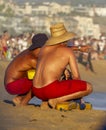 Two lifeguards in red shorts crouched while discussing strategy with crowd in background